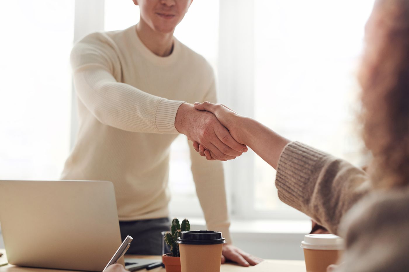 Zwei Personen geben sich bei einem Gespräch am Tisch die Hand