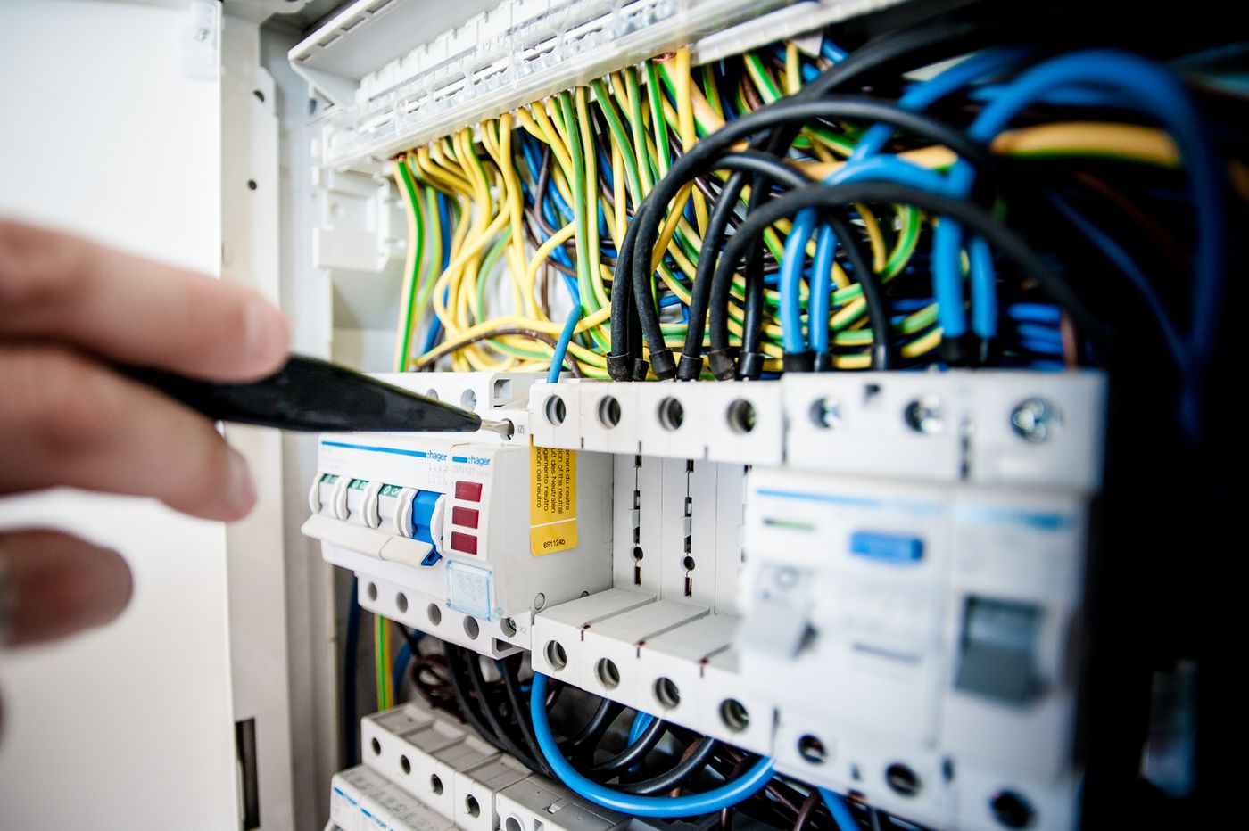 Hand mit Werkzeug an einer elektrischen Verteilung mit Kabeln und Sicherungen