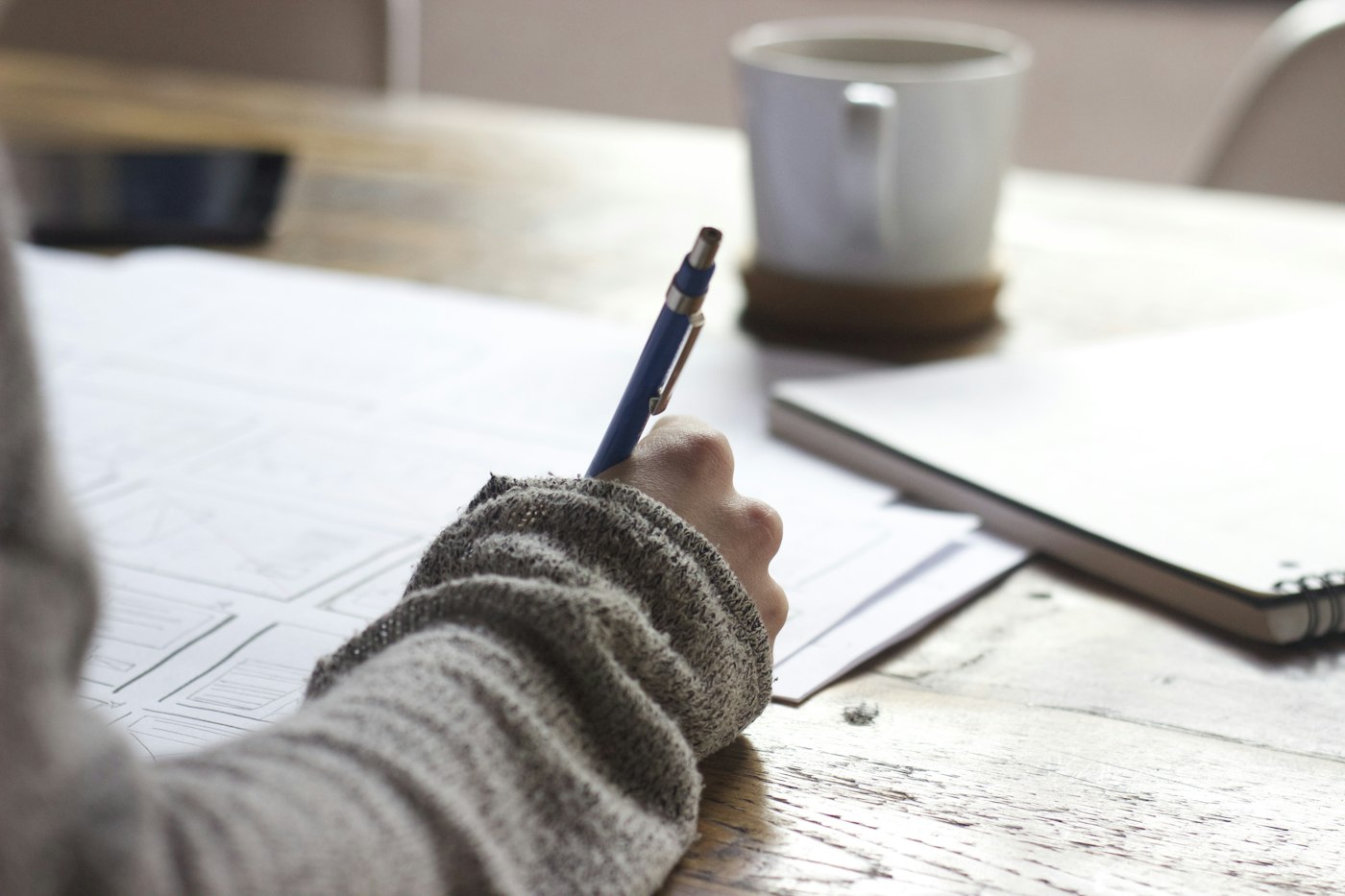 Person macht mit einem Stift Notizen auf Unterlagen am Schreibtisch