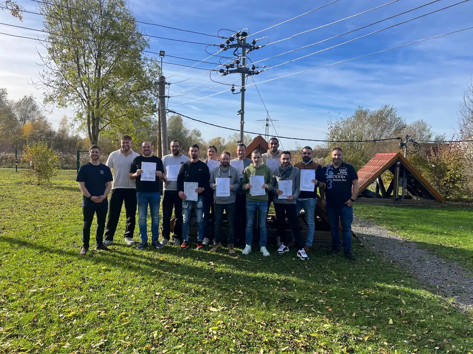 Gruppenfoto zum Abschluss der Qualifizierung mit Teilnehmenden und Zertifikaten auf dem Außengelände.
